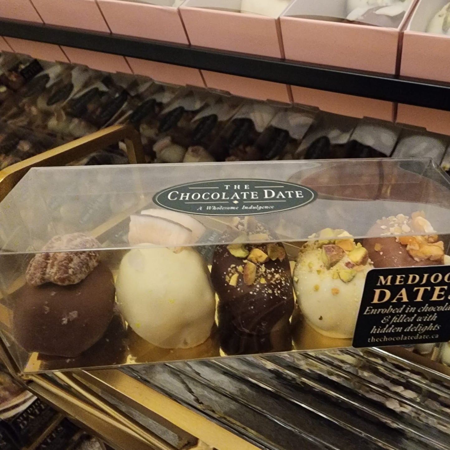 Clear 200 gram box of five assorted chocolate-enrobed Medjool dates with The Chocolate Date label reading "Medjool dates enrobed in chocolate & filled with hidden delights"